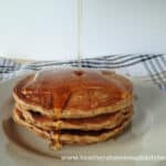 Stack of 3 Whole Wheat Banana Pancakes with drizzle of syrup on white round plate.