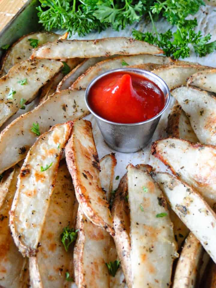 Crispy oven fries on sheet pan around small bowl of ketchup.