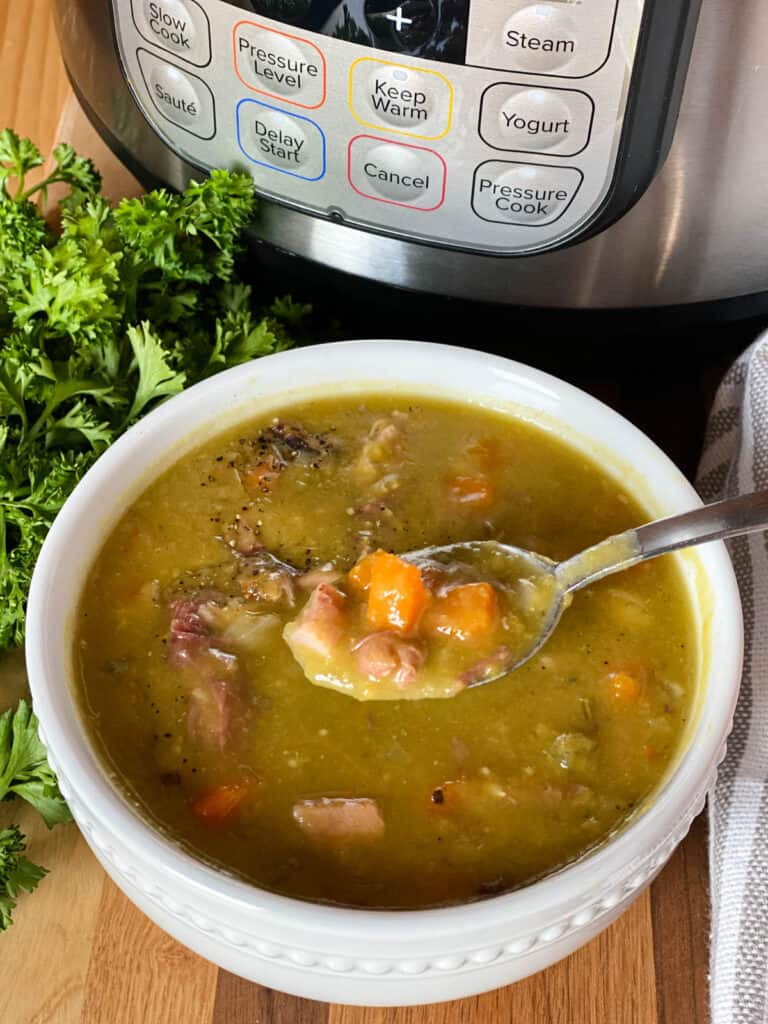 Instant pot split pea soup in white bowl with spoonful in front of instant pot.