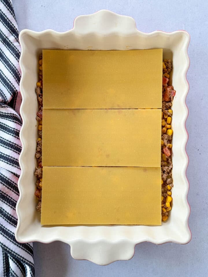 Lasagna pasta sheets on top of the sauce in caserole dish.