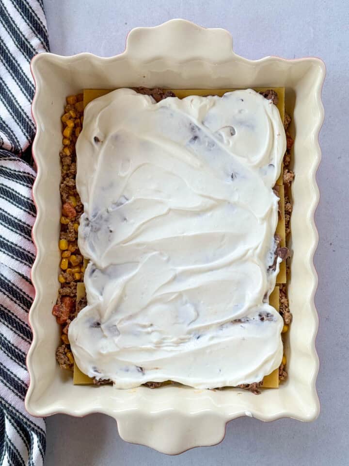 Layer of sour cream spread over refried black beans in casserole dish.