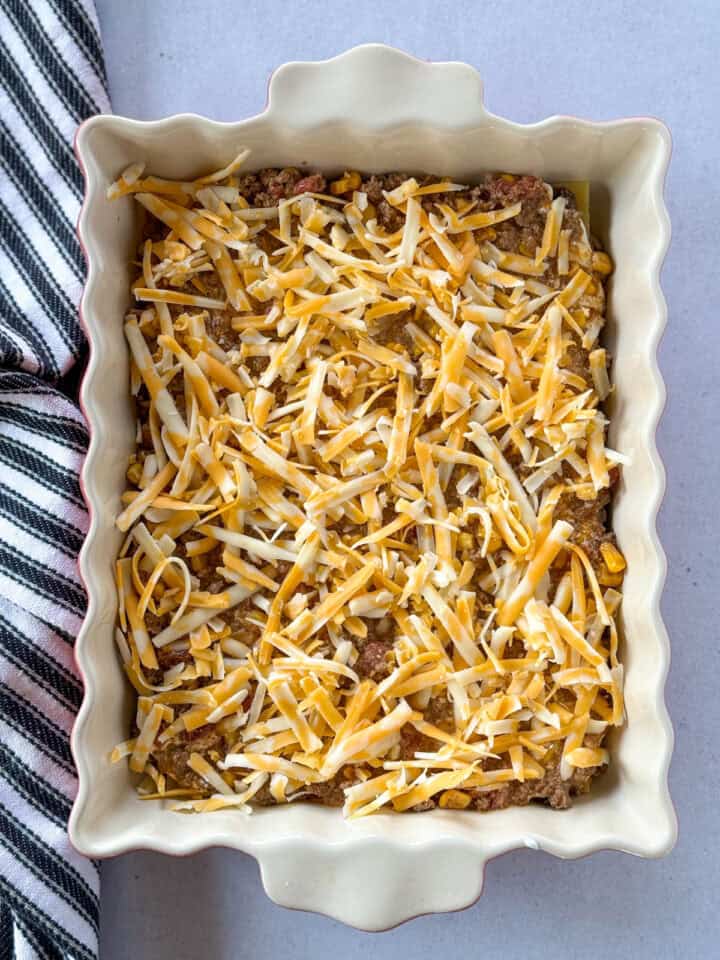 Shredded cheese on top of sauce in casserole dish.