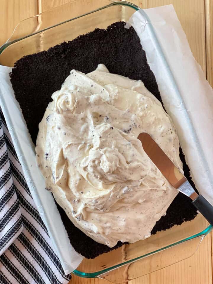 Cheesecake layer being spread on top of cookie crust with offset spatula.