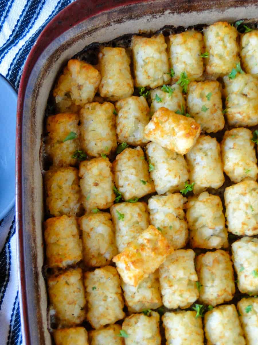 Top close up view of tater tot hotdish in casserole dish with serving spoon on the side.