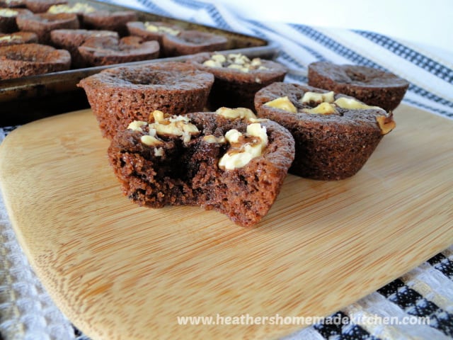 Homemade Brownie Bites with chopped walnuts on top sitting on bamboo board with a bite taken. 