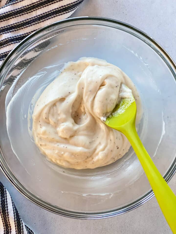 Dressing ingredients combined in large glass bowl with green spatula.