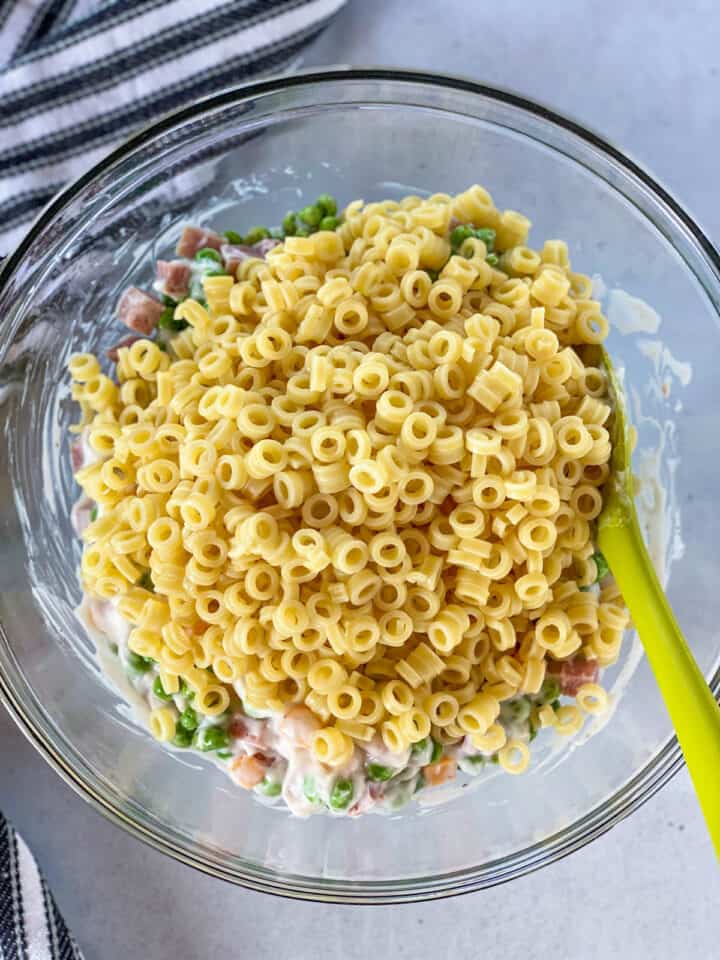 Rinsed and cooled pasta added to dressing and other ingredients in large glass mixing bowl.