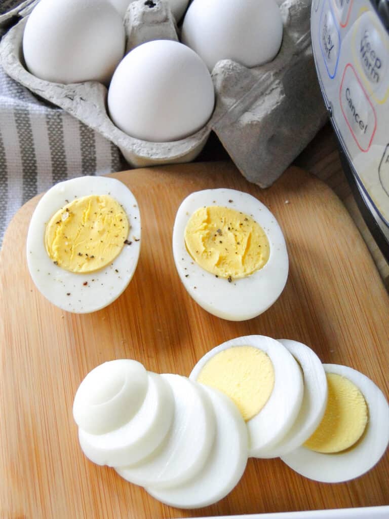 Top view of Instant pot hard boiled egg sliced in half on board and an egg sliced with an egg slicer.