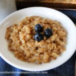 Instant Pot Maple Brown Sugar Oatmeal in white bowl garnished with blueberries on spoon sitting on the side of bowl.