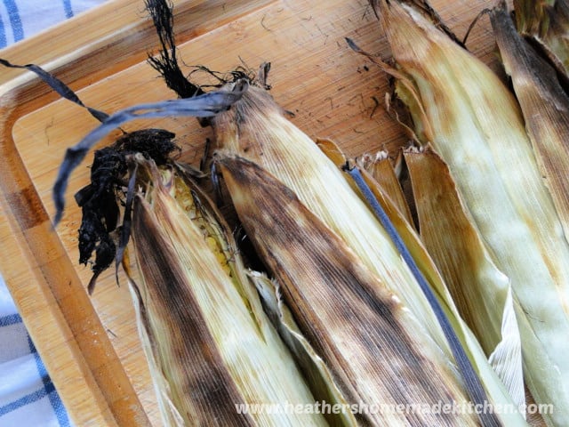 Three Oven Roasted Corn with Husks on top of bamboo board cooling. 