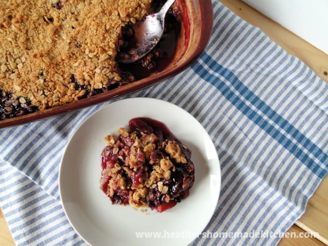Top view of Very Berry Apple Crisp in baking dish with a serving on a white plate.