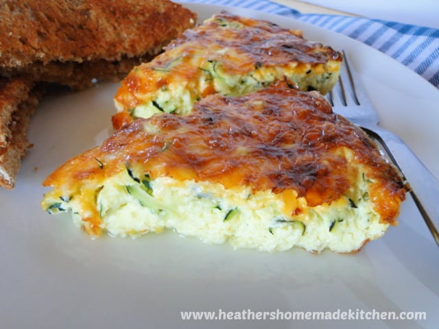 Side view of two slices of Zucchini Frittata on white plate with fork on right side and slice of toast on left side.