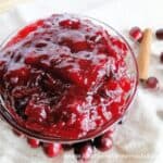 Fresh Cranberry Sauce in glass bowl with cinnamon stick and scattered cranberries.