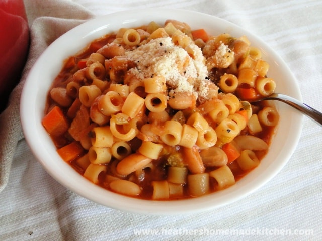 Pasta E Fagioli in white bowl with spoon and grated Parmesan cheese on top.