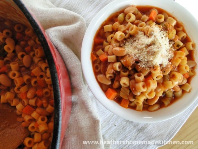 Pasta E Fagioli in bowl with parmesan cheese on top next to pot of soup.