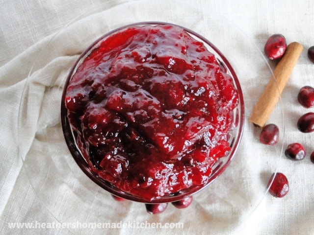 Top view of fresh cranberry sauce in glass bowl with cinnamon stick and scattered cranberries. 