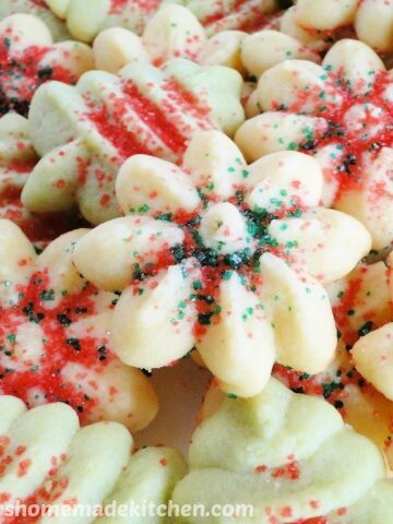 Spritz Butter Cookies shaped as green trees and white flowers and sprinkled with green and red sugar.