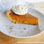 Side view of Homemade Pumpkin Pie Recipe with whipped cream and sprinkle of cinnamon on white round plate.