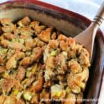 Homemade Stuffing in casserole dish with spoonful on wooden spoon.