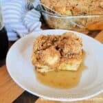 French Toast Casserole slice on white round plate with maple syrup on top.