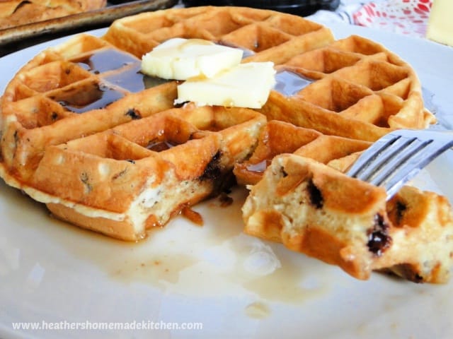 Close up view of homemade chocolate chip waffles with pats of butter, syrup and a bite on a fork.
