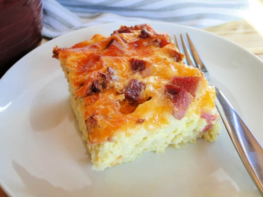 Slice of best ever egg bake with hashbrowns on white round plate with fork. 