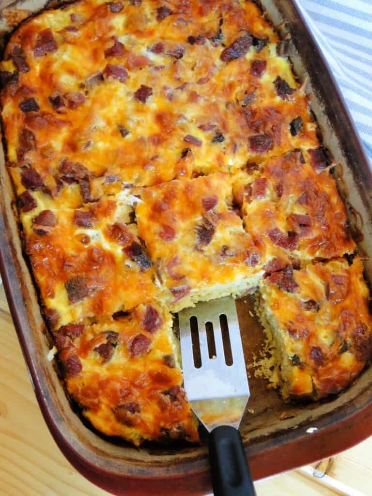 Golden brown best ever egg bake sliced in casserole dish with spatula. 