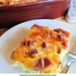 Best ever egg bake slice on white round plate with fork in front of casserole dish of egg bake.