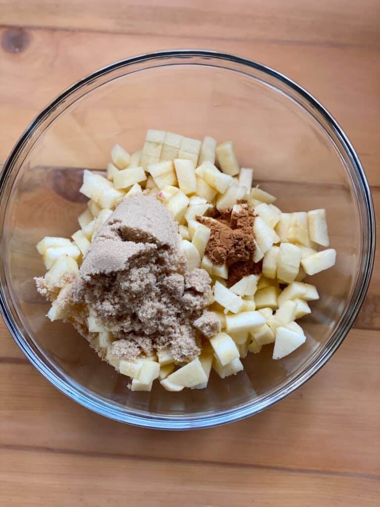 Diced apples with brown sugar and cinnamon in a small glass mixing bowl.