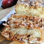 Slices of apple fritter bread in front of loaf on board with bread knife.
