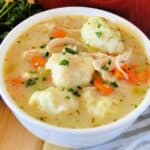 Chicken dumpling soup in white bowl in front of red pot of soup.