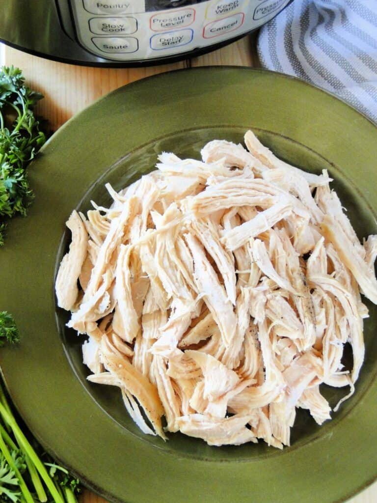 Instant pot shredded chicken on green round platter in front of instant pot.