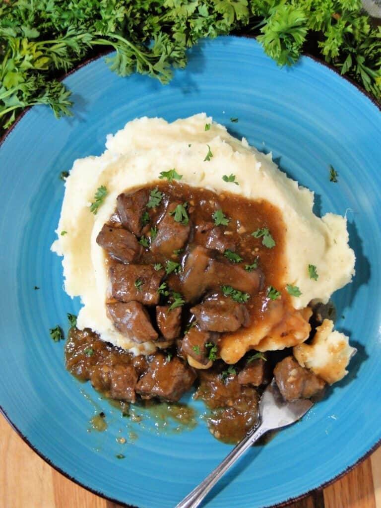 Top view of instant pot beef tips with gravy served over mashed potatoes on a blue plate.