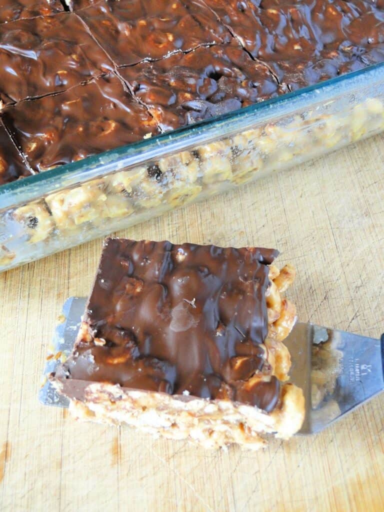 Top view of no bake peanut butter cereal bars with one cut out and on spatula on a board. 