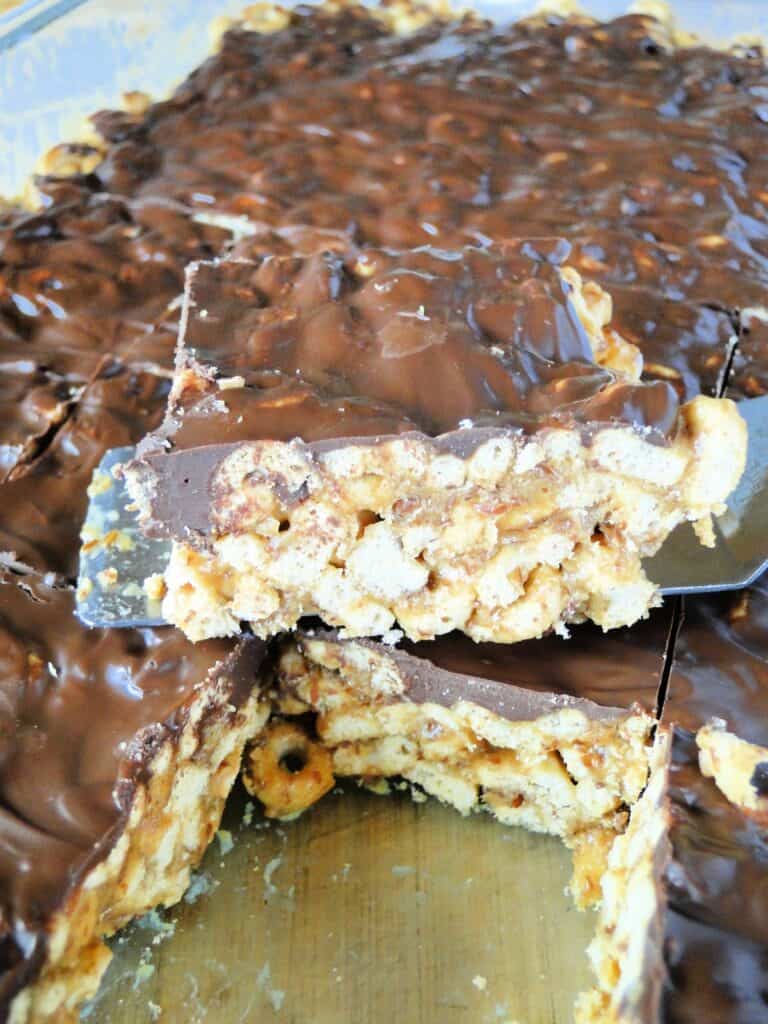 Baking dish of no bake peanut butter cereal bars, sliced and one slice on a spatula. 