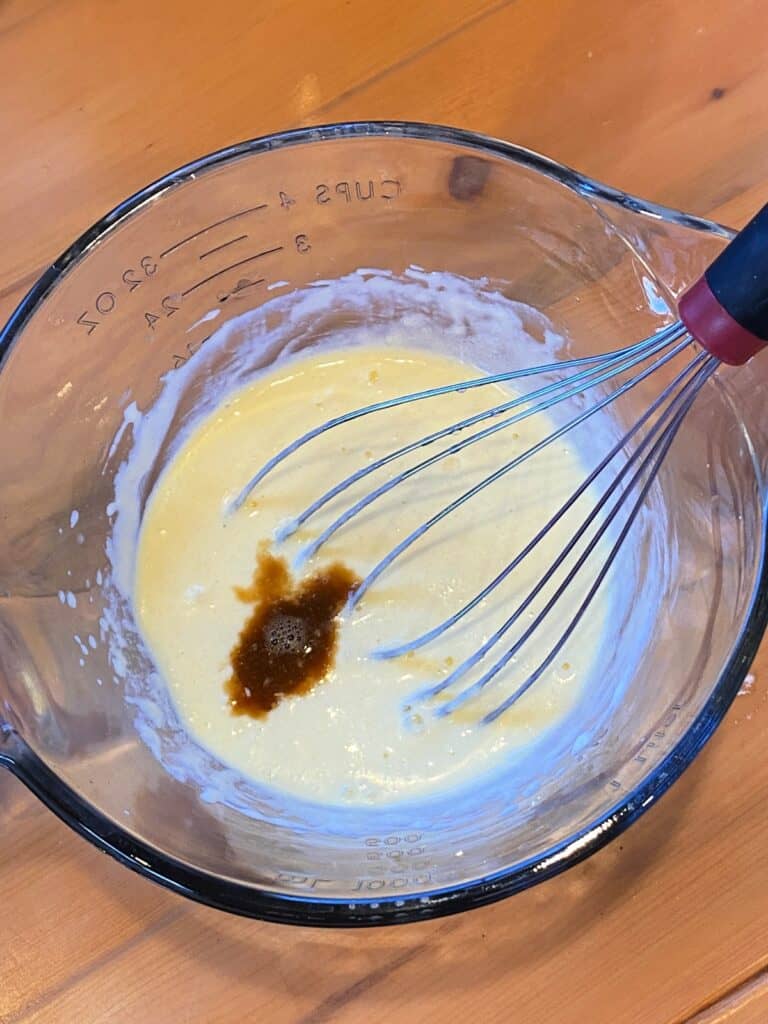 Wet ingredients in mixing bowl with whisk and drizzle of vanilla extract. 