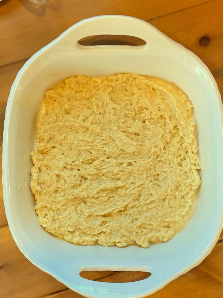Half of the coffee cake batter spread into a white 8x8 baking dish. 