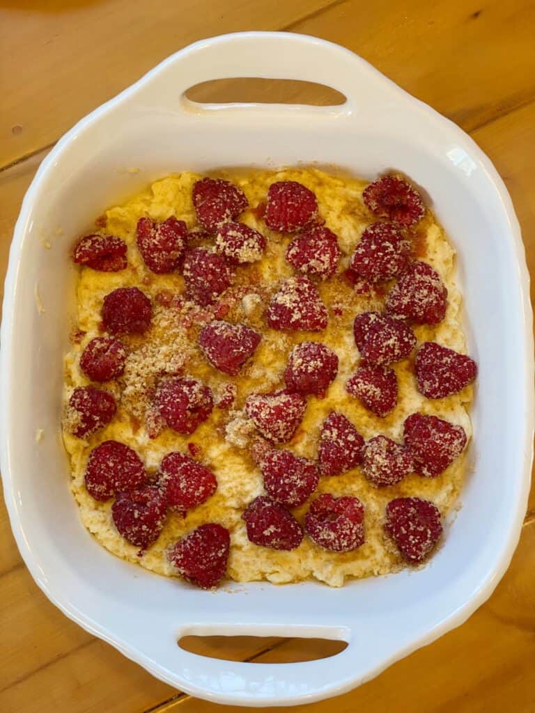 Sugared raspberries on top of coffee cake batter in white 8x8 baking dish.
