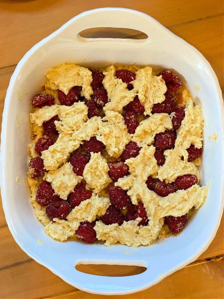 Coffee cake batter on top of sugared raspberries in 8x8 white baking dish.