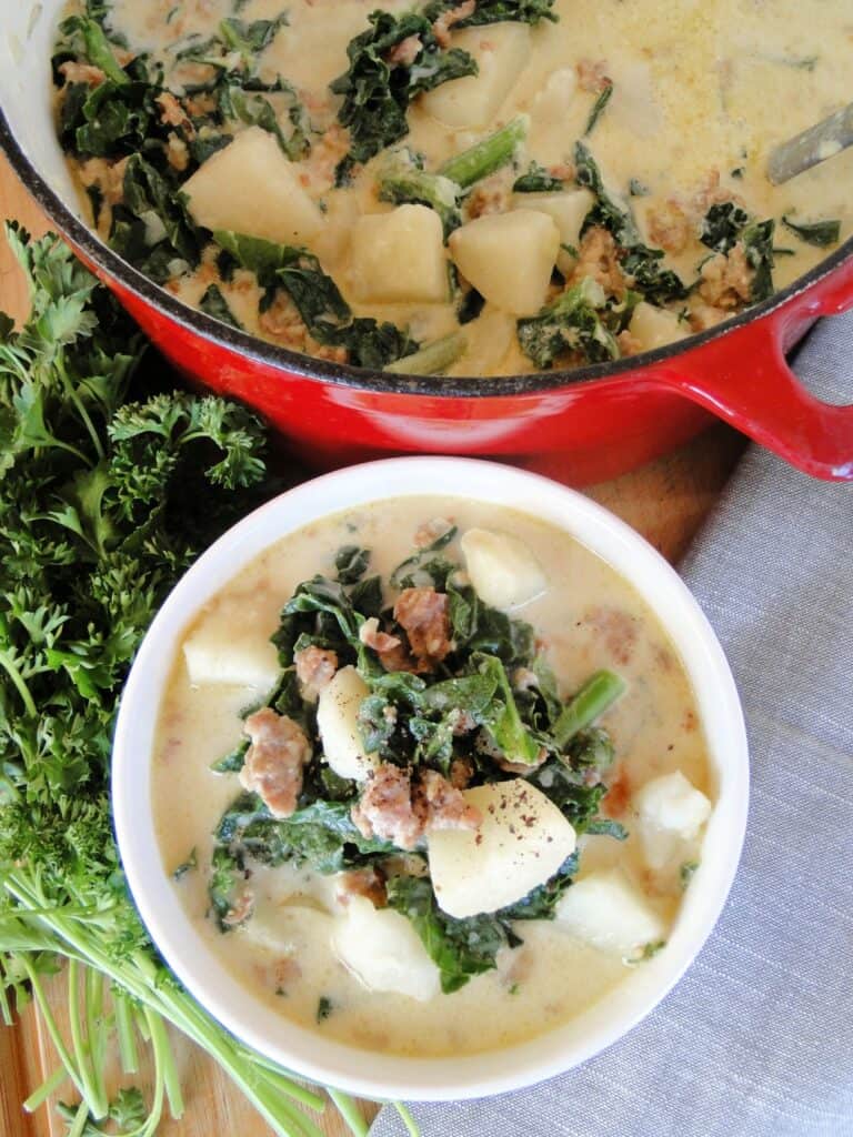 Top view of Easy Zuppa Toscana Soup in white bowl and red dutch oven with ladle. 