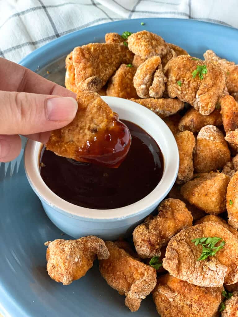 Air fryer chicken nugget being dipped in BBQ sauce.