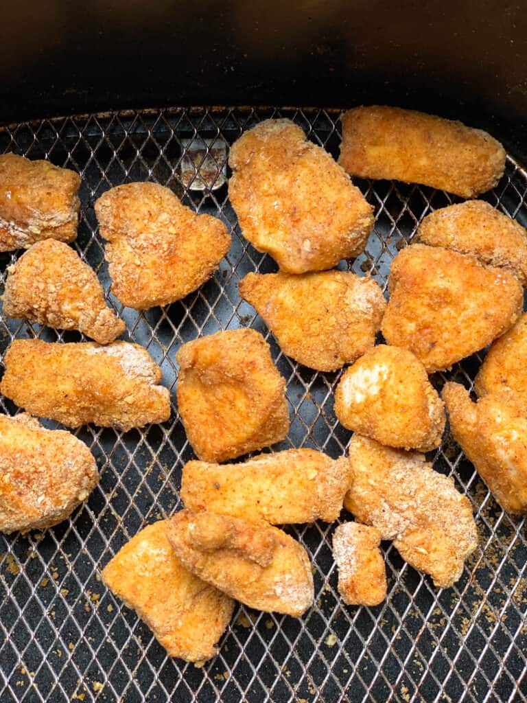 Half way cooked chicken bites in air fryer basket.