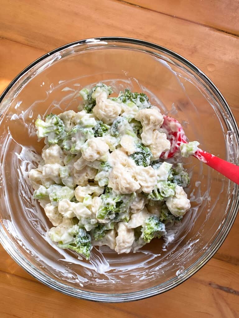 Broccoli and cauliflower florets mixed with homemade dressing in glass bowl.