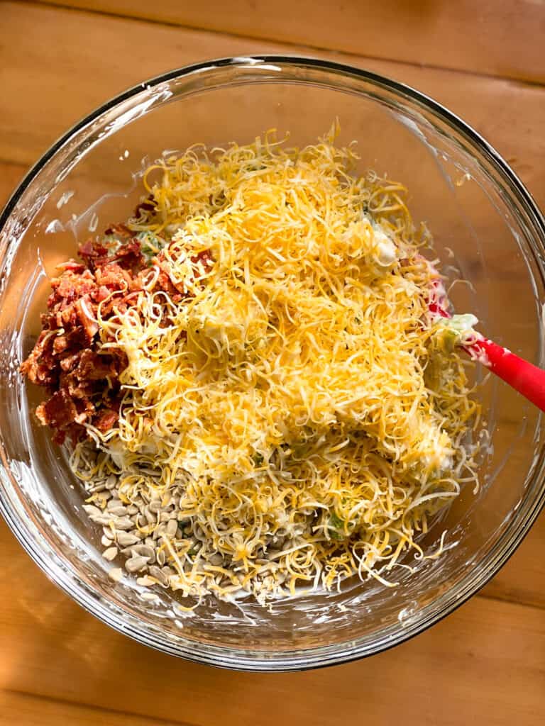 Last step in making salad, adding crumbled bacon, shredded cheese and sunflower seeds.