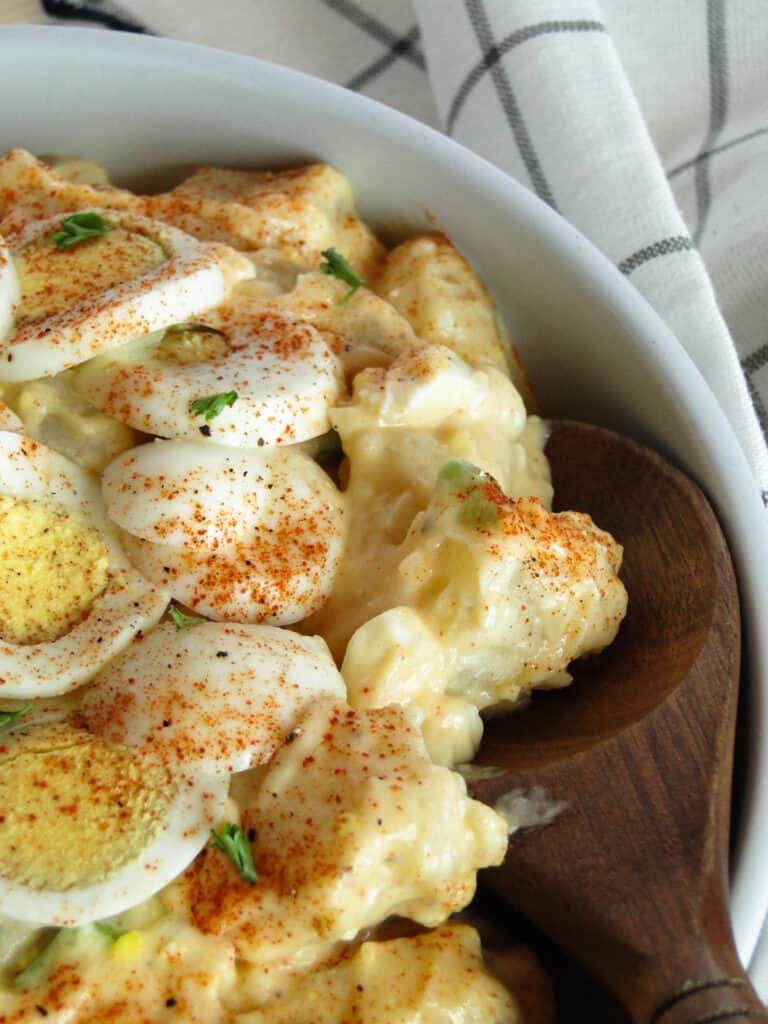 Close up view of classic potato salad in white bowl with wood serving spoon.