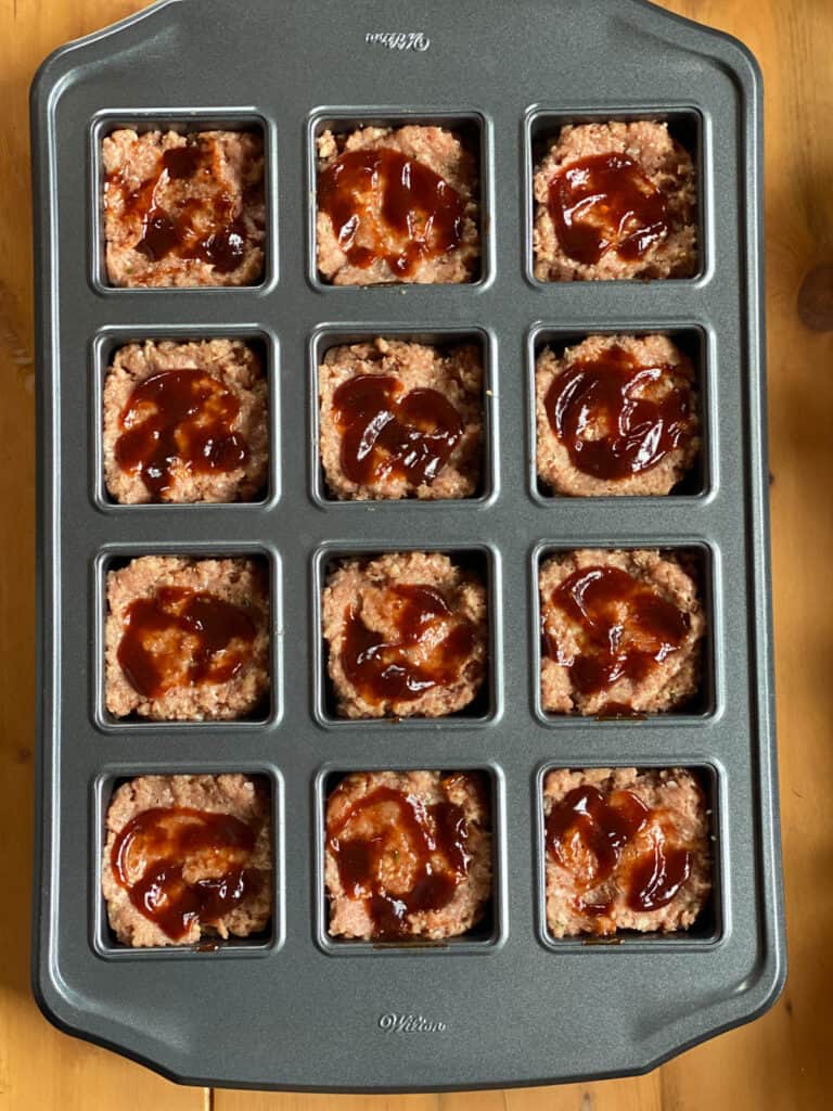 Mini bbq turkey meatloaves pressed into brownie pan with bbq spread on top of each one.