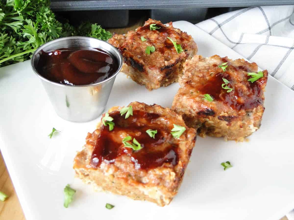 Mini bbq turkey meatloaves on square with plate with extra bbq sauce in sauce cup.