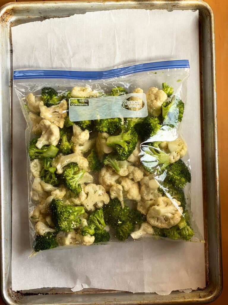 Broccoli and cauliflower combined with oil and seasonings in zip top bag.