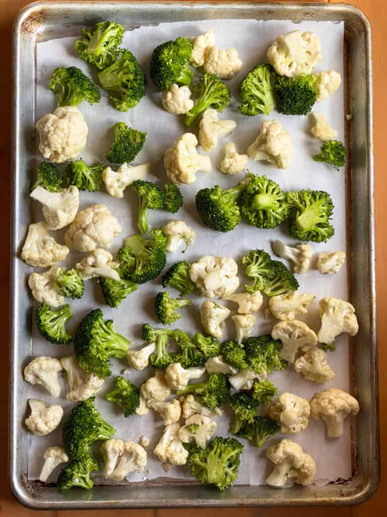 Oil and seasoned broccoli and cauliflower spread out on sheet pan.
