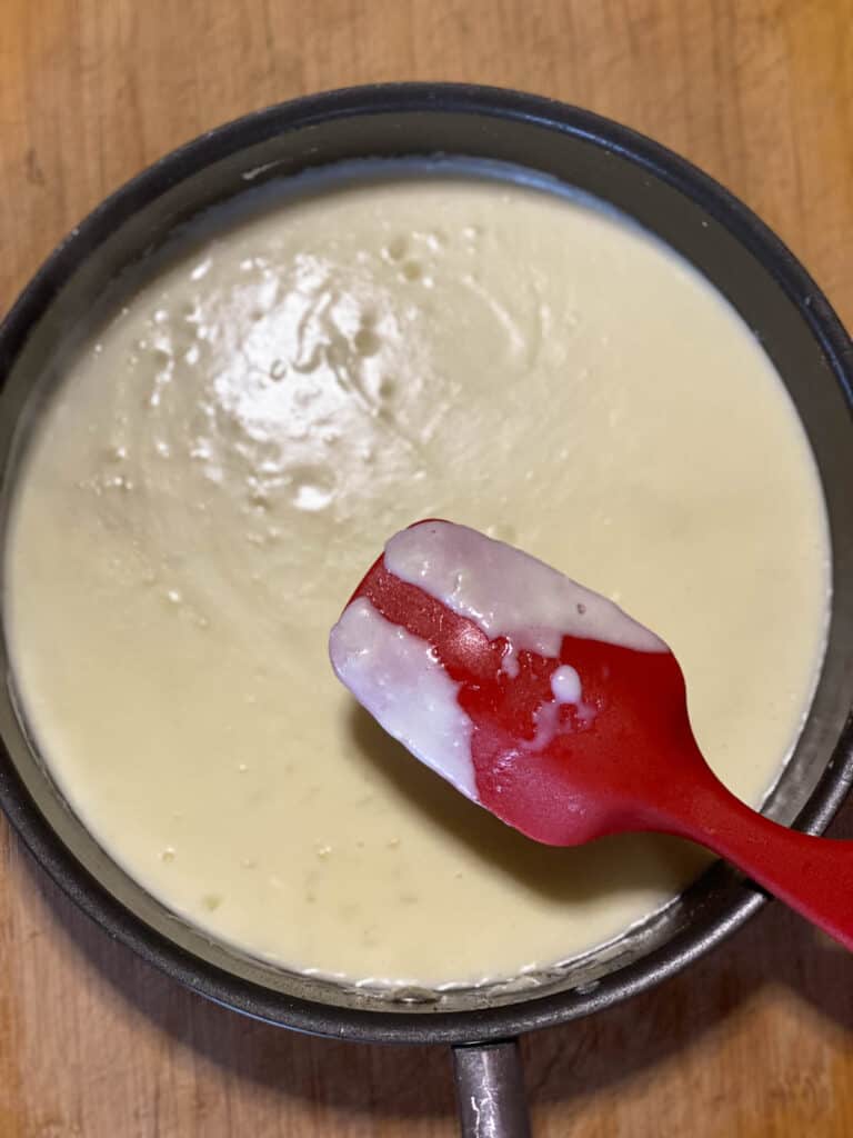 Thickened béchamel sauce in sauce pan coating the back of a spoon..
